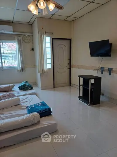 Spacious bedroom with multiple beds, wall-mounted TV, and modern ceiling fan.