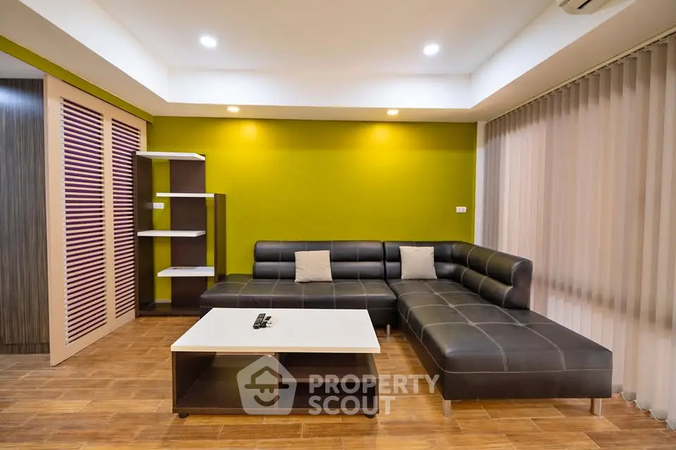 Modern living room with stylish black leather sectional sofa and sleek wooden flooring.