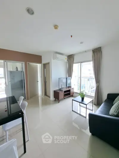 Modern living room with sleek furniture and natural light, featuring a TV and balcony access.