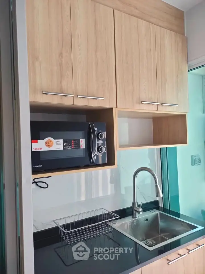 Modern kitchen with sleek cabinetry, stainless steel sink, and built-in microwave in a compact layout.