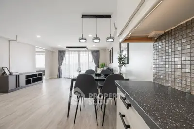 Spacious modern living room with dining area and stylish kitchen, featuring elegant lighting and large windows.