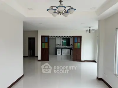 Spacious open-plan living area with modern lighting and tiled flooring, leading to a stylish kitchen.