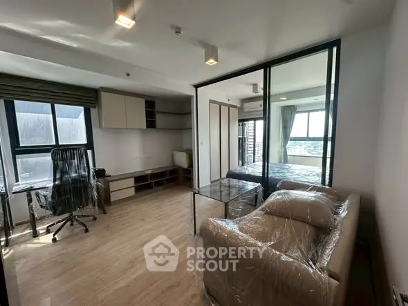 Modern studio apartment with glass partition, stylish furniture, and city view.