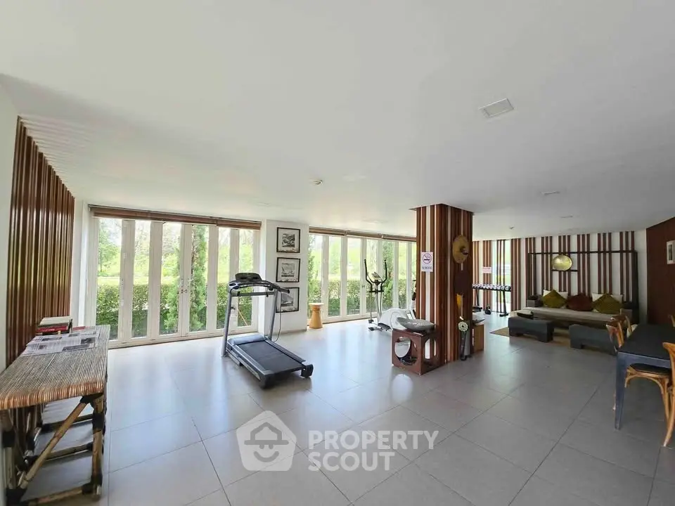Spacious fitness room with modern equipment and large windows offering garden views.