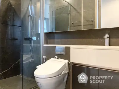 Sleek modern bathroom with glass shower enclosure and dark marble tiles, featuring a stylish vanity and high-end fixtures.