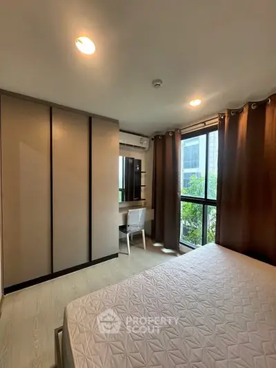 Modern bedroom with large window and built-in wardrobe in urban apartment.