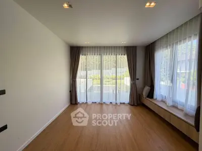 Spacious living room with large windows and elegant curtains, offering a serene garden view.