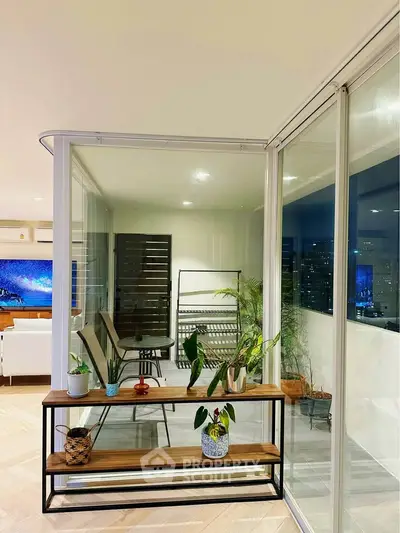 Modern apartment with glass-enclosed balcony offering stunning city views and stylish interior decor.