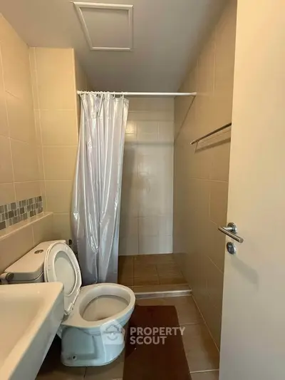 Modern bathroom with shower and toilet in a minimalist design, featuring neutral tiles and a sleek sink.