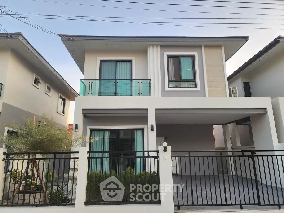 Modern two-story house with balcony and gated driveway in suburban neighborhood.