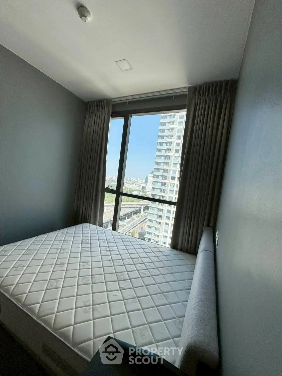 Modern bedroom with large window and city view, featuring a comfortable bed and stylish decor.