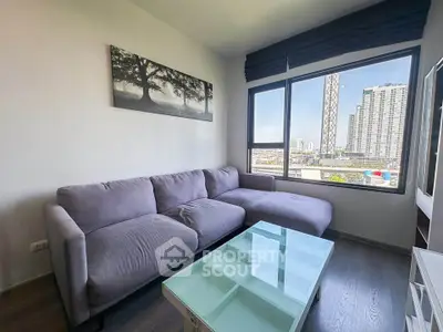 Modern living room with large window and city view, featuring a stylish gray sofa and glass coffee table.