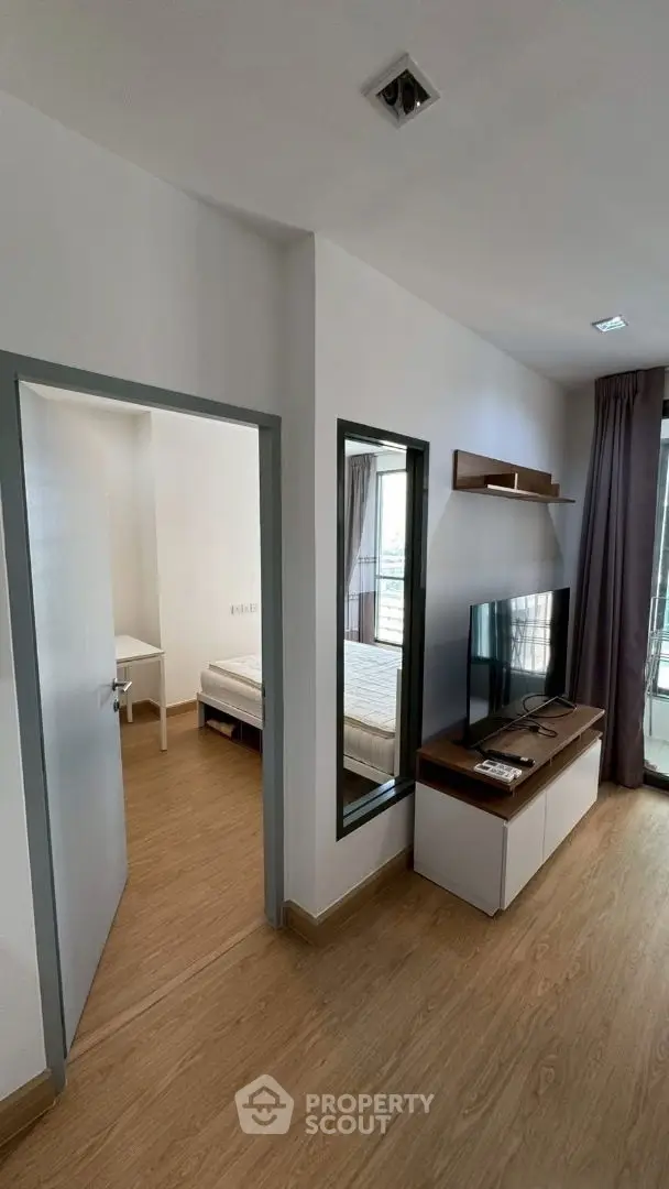 Modern living room with TV and wooden flooring, adjacent to a cozy bedroom.