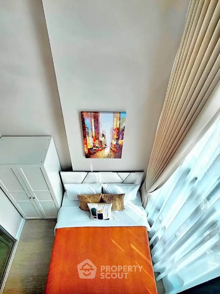 Modern bedroom with vibrant orange bedding and large window for natural light.