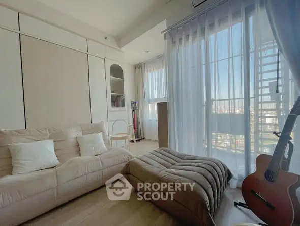 Cozy living room with plush seating and guitar, featuring large windows and sheer curtains.