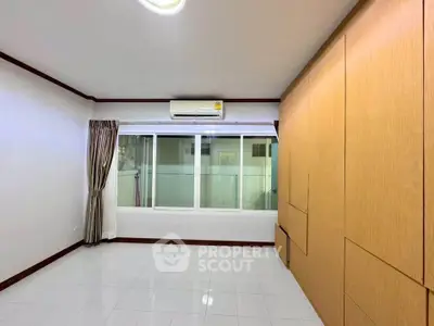 Spacious room with large window and built-in wooden wardrobe, perfect for modern living.