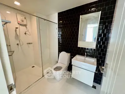 Sleek modern bathroom with glass shower enclosure, black tiled walls, and white fixtures, offering a clean and contemporary look.