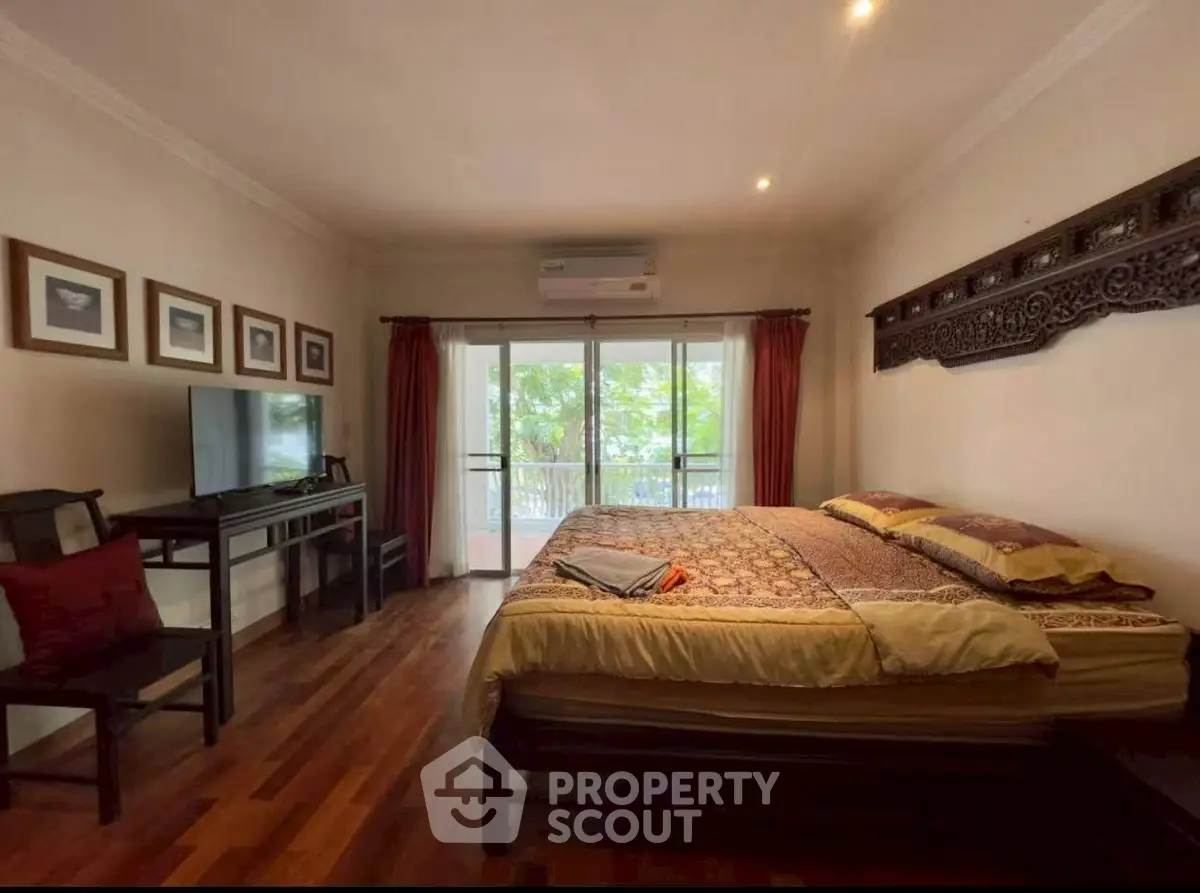 Spacious bedroom with elegant decor and balcony view, featuring hardwood floors and stylish furniture.