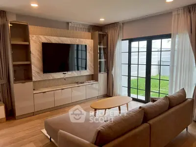 Modern living room with large TV, stylish sofa, and garden view through glass doors.