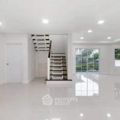 Spacious modern living room with glossy tile flooring and staircase, featuring large windows for natural light.