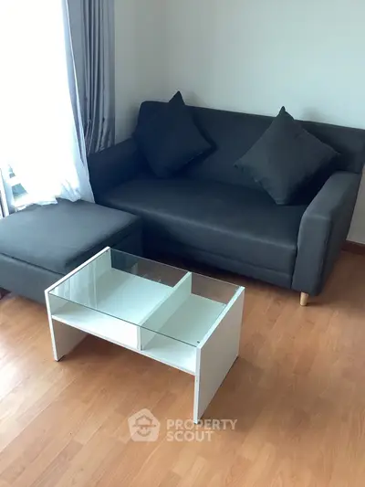 Cozy living room with modern gray sofa and glass coffee table on wooden floor.