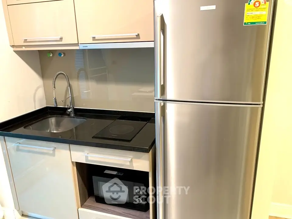 Modern kitchen with sleek appliances and compact design, featuring a stainless steel fridge and built-in microwave.