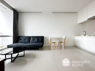 Sleek modern studio apartment with integrated living space, featuring a stylish black sofa, minimalist dining set, and a clean white kitchenette.