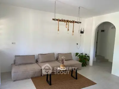 Modern minimalist living room with cozy sofa and unique hanging light fixture.