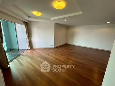 Spacious empty living room with wooden flooring and balcony access