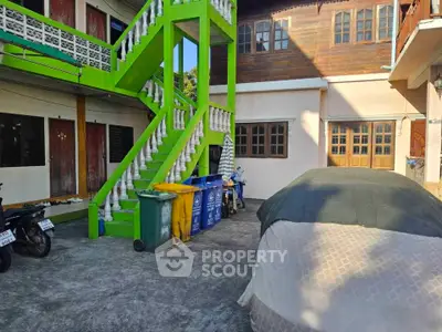 Charming exterior view of a traditional building with vibrant green staircase and covered parking area.