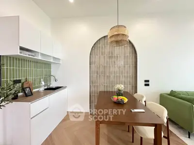Modern kitchen with open layout and stylish dining area featuring green accents and wooden furniture.