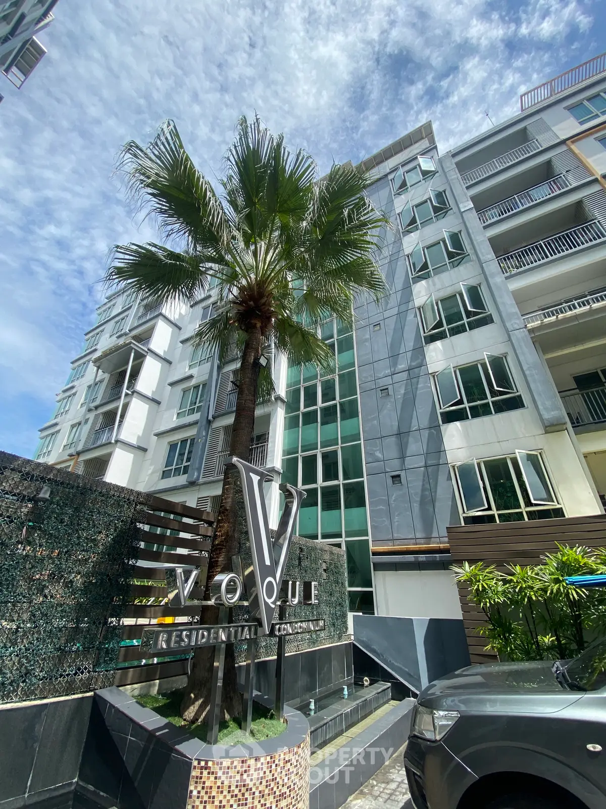 Modern residential condominium with palm tree and sleek facade under blue sky.