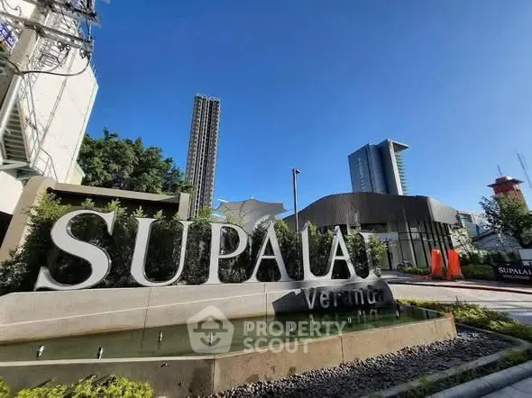 Modern urban building exterior with Supalai signage and lush landscaping under clear blue sky.