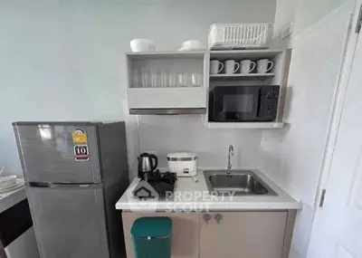 Modern compact kitchen with stainless steel fridge, microwave, and sink in a stylish apartment.