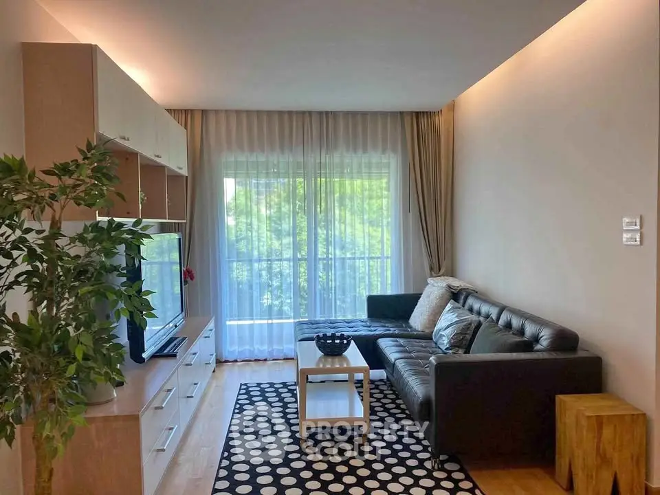 Modern living room with sleek black sofa, stylish decor, and large window offering natural light and greenery view.