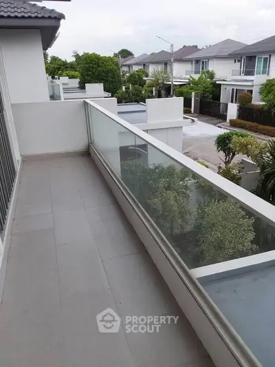 Spacious balcony with glass railing offering a serene neighborhood view, perfect for relaxation and outdoor enjoyment.