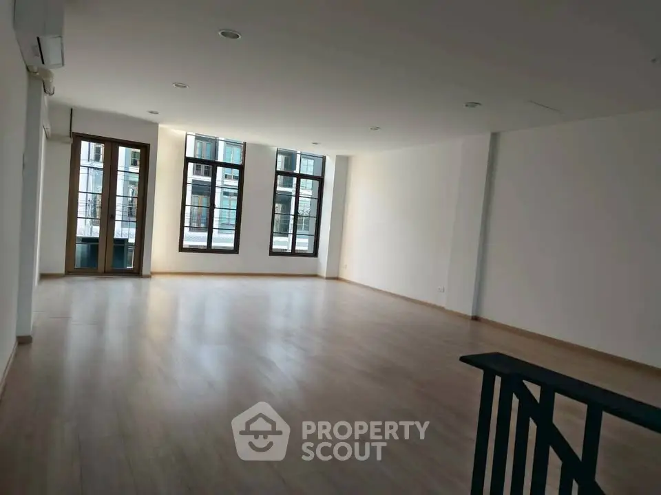 Spacious empty living room with large windows and wooden flooring in modern apartment.