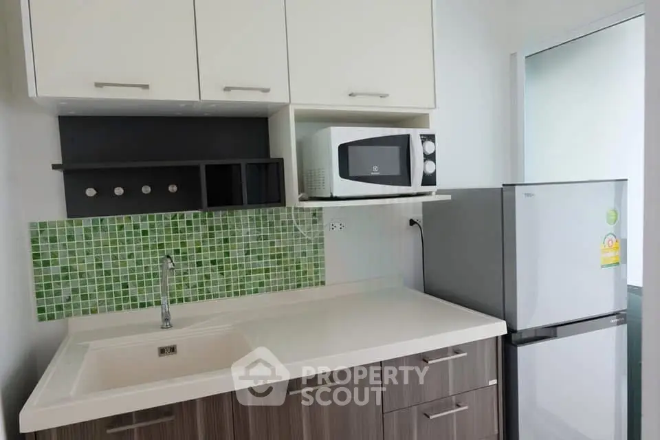 Modern kitchen with sleek cabinetry, microwave, and fridge in a compact layout.