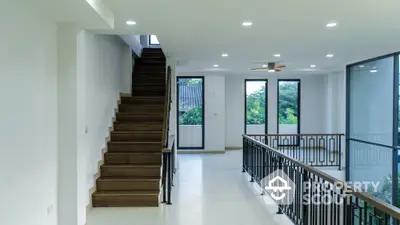 Spacious modern hallway with wooden staircase and large windows offering natural light.