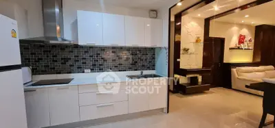 Modern kitchen with sleek white cabinets and open layout leading to stylish living room.