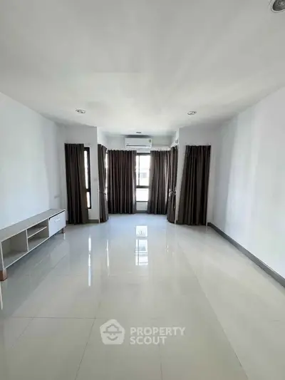 Spacious unfurnished living room with large windows and sleek tile flooring.