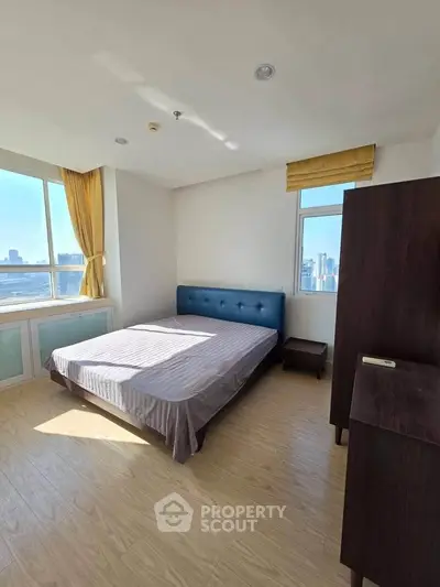 Bright bedroom with city view and modern furnishings, featuring a large window and wooden flooring.