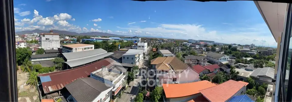 Panoramic cityscape view from a high-rise building showcasing diverse rooftops and distant mountains.