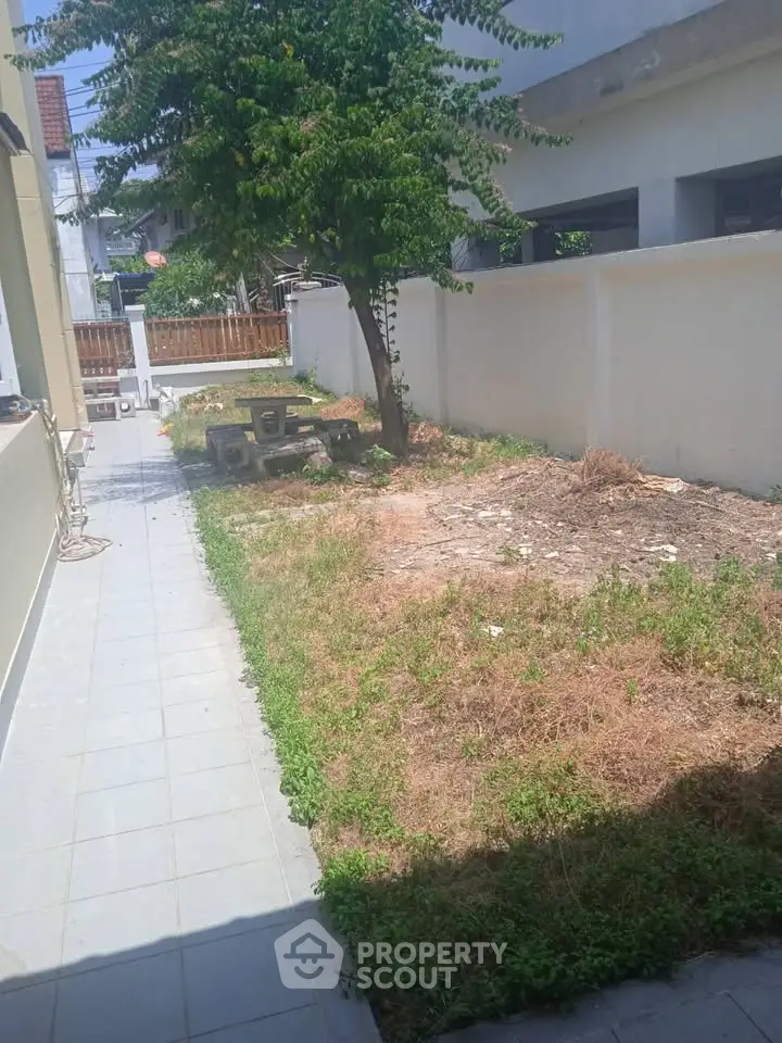 Charming outdoor garden space with potential for landscaping, featuring a tree and paved walkway.