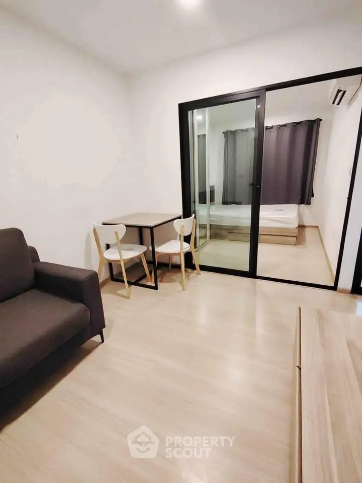 Modern living room with sliding glass doors leading to a cozy bedroom, featuring minimalist furniture and neutral tones.