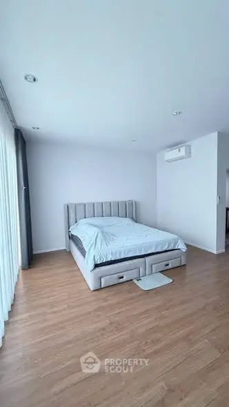 Spacious bedroom with modern decor and natural light, featuring a comfortable bed and sleek wooden flooring.
