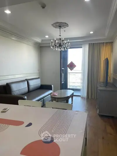 Modern living room with chandelier and balcony view, featuring stylish furniture and elegant decor.