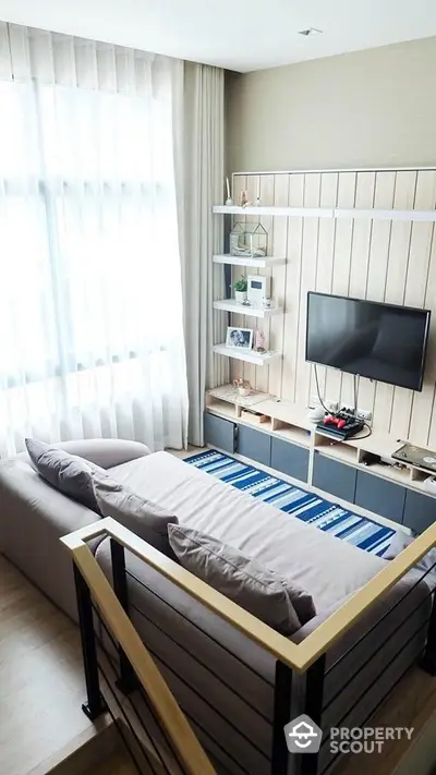 Modern minimalist bedroom with a cozy single bed, sleek wall-mounted TV, and elegant shelving, bathed in natural light from the sheer curtains.