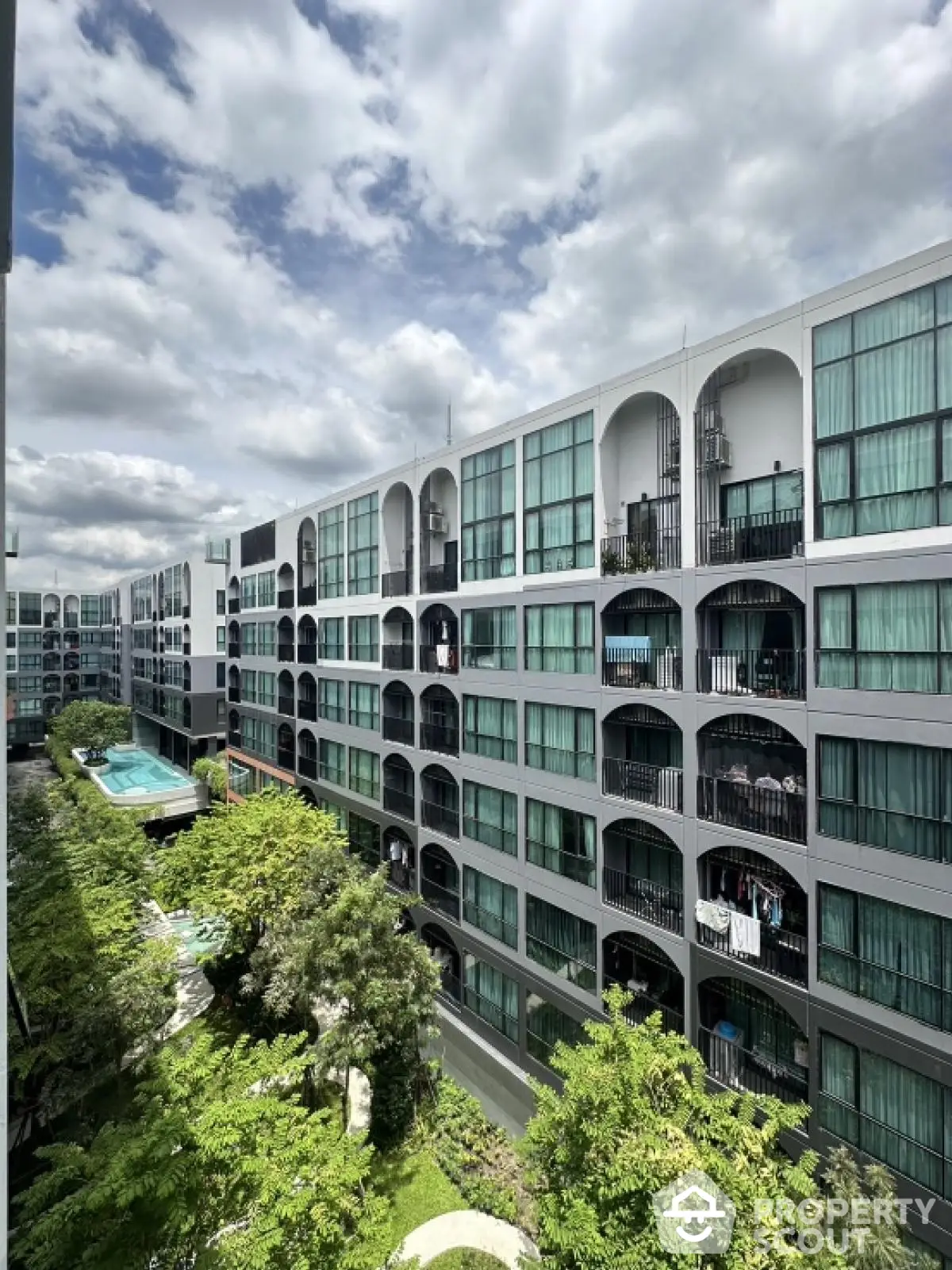 Modern apartment complex with pool and lush greenery under a cloudy sky