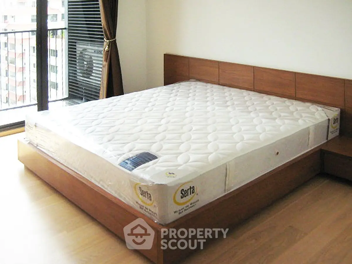 Spacious bedroom with large window and modern wooden bed frame, perfect for comfort and relaxation.